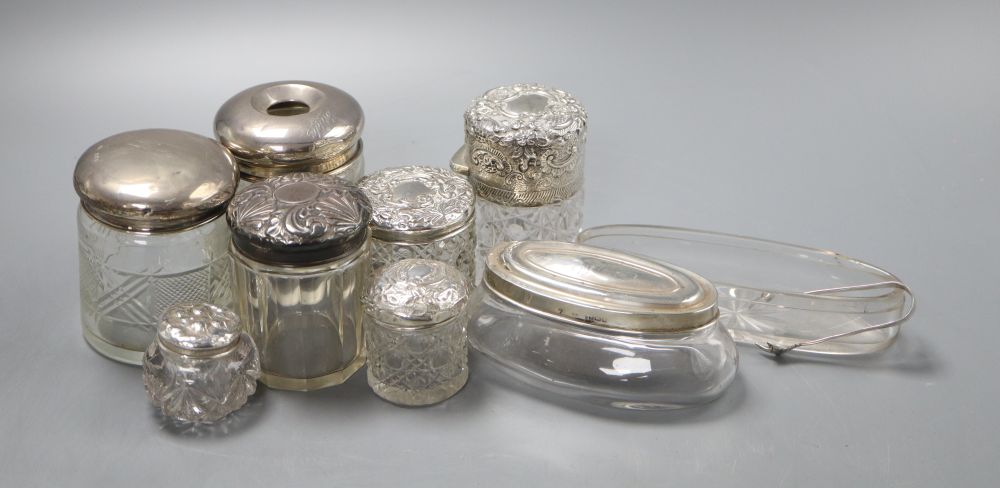 Eight assorted silver lidded glass toilet jars, a further glass jar lacking lid and a small pair of silver tongs